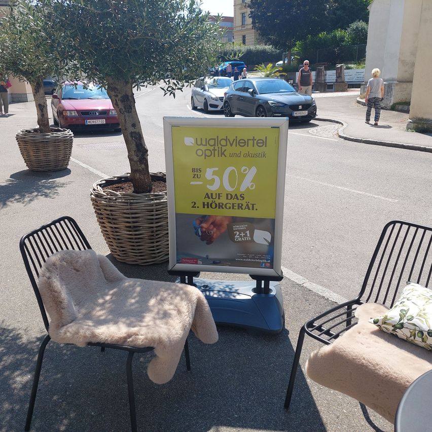 Ein Schild mit einer Werbung für bis zu 50% Rabatt neben zwei Stühlen, mit Bäumen und Autos im Hintergrund.