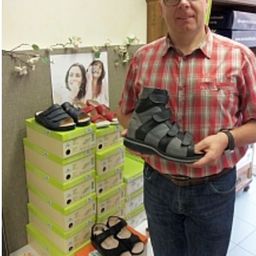 Ein Mann mit Brille hält einen Schuh in der Hand. Er steht vor einem Stapel Schuhe.