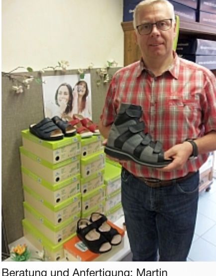 Ein Mann mit Brille hält einen Schuh in der Hand. Er steht vor einem Stapel Schuhe.