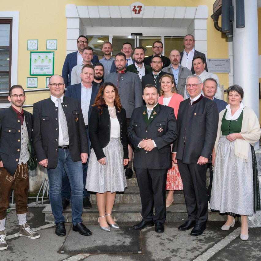 Eine Gruppe von Menschen in traditioneller deutscher Kleidung posiert für ein Foto auf den Stufen eines Gebäudes mit gelben Wänden.