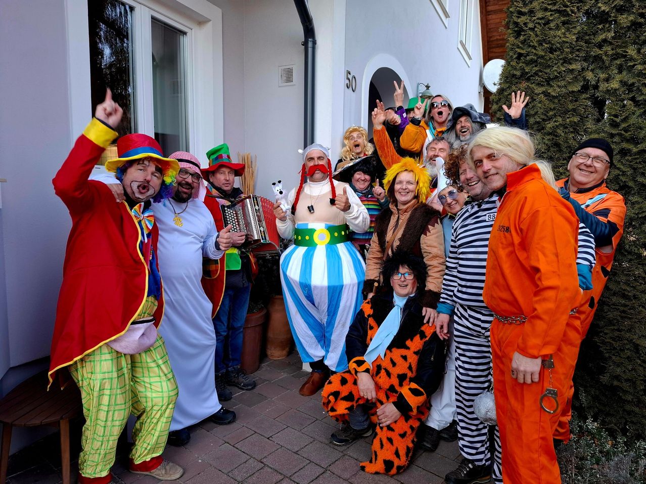 Eine Gruppe von Menschen in verschiedenen Kostümen posiert für ein Foto vor einem Gebäude. Sie lächeln und machen lustige Gesten.