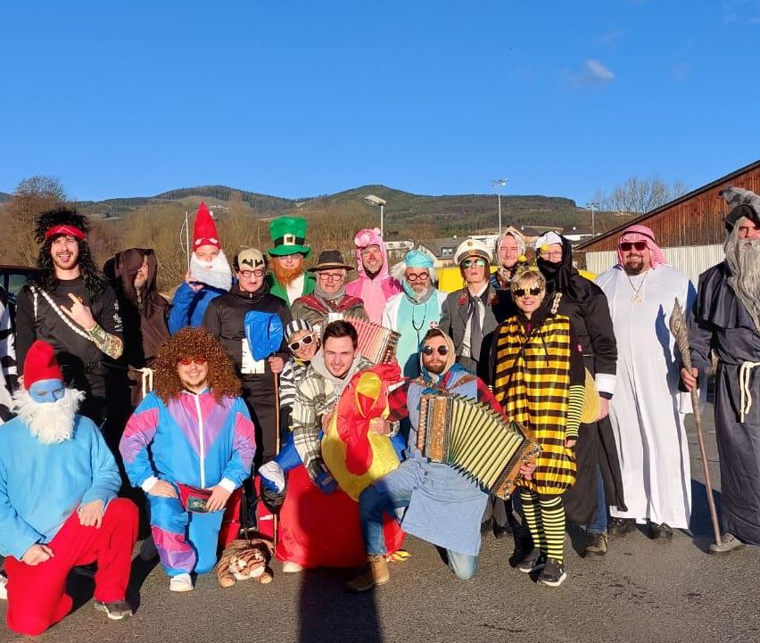 A group of people in various costumes pose for a photo in an outdoor area with mountains in the background.
