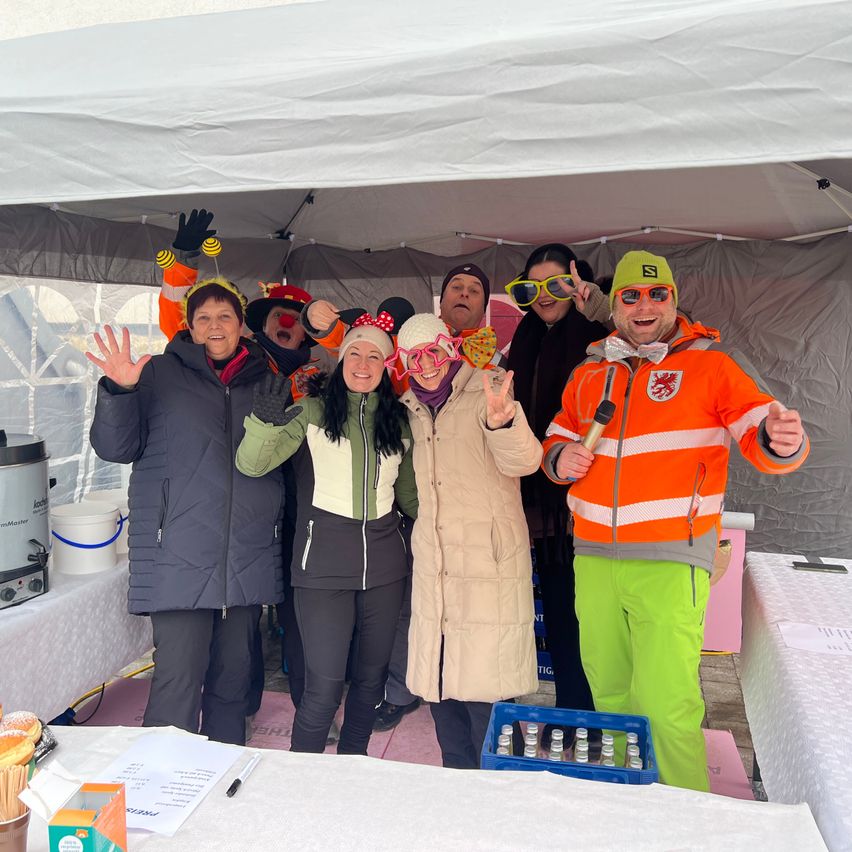 Eine Gruppe von Menschen in Kostümen posiert für ein Foto in einem Zelt, vor ihnen steht ein Tisch.