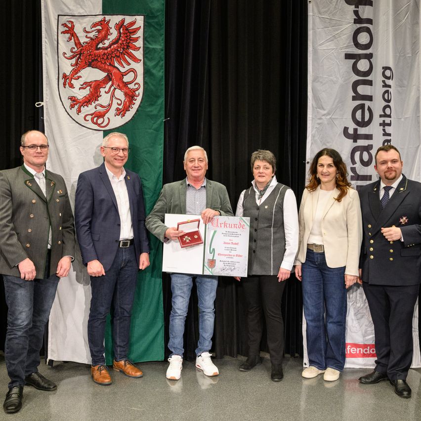 Eine Gruppe von Menschen in formeller Kleidung steht vor einem Banner mit dem Text 'rafendorf' und einem Logo. Ein Mann hält ein Zertifikat in der Hand.