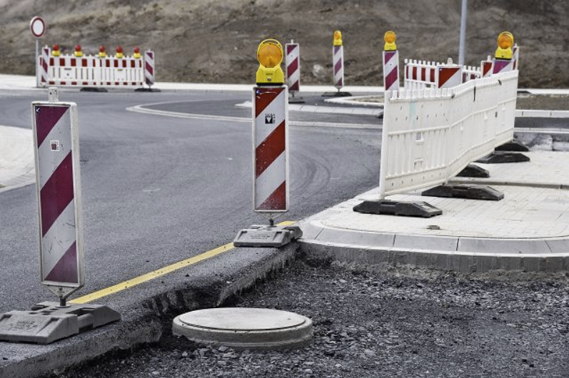 Eine Straße im Bau mit Barrieren, Verkehrskegel und einem Schachtdeckel an der Seite.