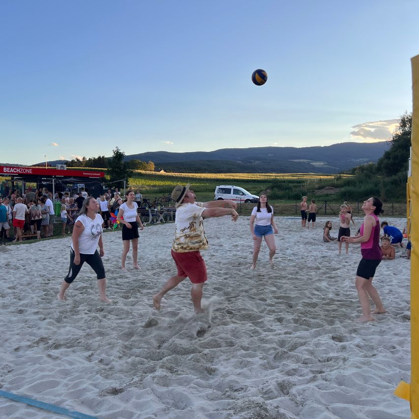 A group of people playing beach volleyball on a sandy beach with mountains in the background.