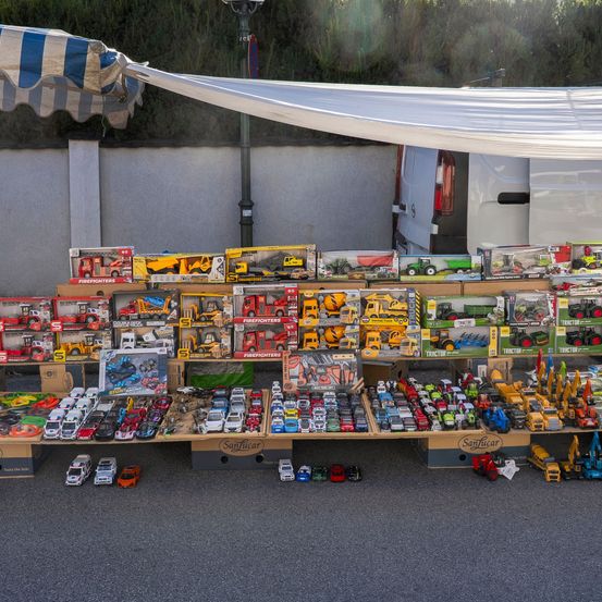 Ein Tisch voller verschiedener Spielzeugfahrzeuge, darunter Autos, Lastwagen und Maschinen, unter einem weißen Baldachin.