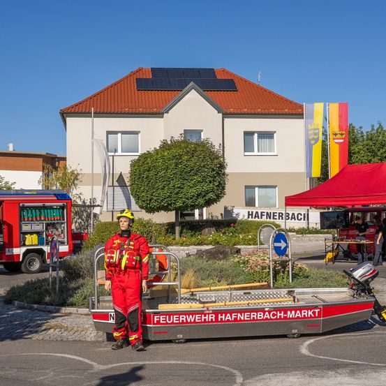 Ein Feuerwehrmann steht neben einem Boot auf der Straße vor einem Haus mit Solarmodulen auf dem Dach.