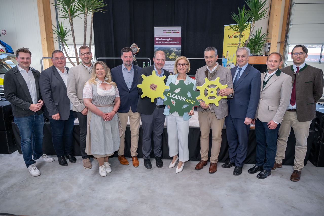Eine Gruppe von Menschen steht in einer Reihe und posiert für ein Foto mit zwei grünen Zahnrädern vor ihnen. Sie sind wahrscheinlich bei einer Veranstaltung.