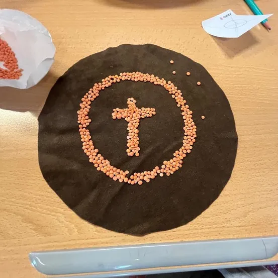 Ein brauner runder Stoff mit einem Kreuz aus roten Linsen in der Mitte, auf einem Holztisch platziert.