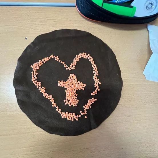 Ein schwarzer runder Stoff mit einem Herz- und einem Kreuzdesign aus rosa Perlen liegt auf einem Holztisch.