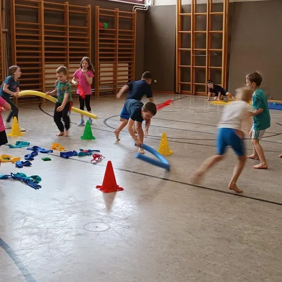 Kinder spielen mit Hula-Hoops und Kegeln in einer Turnhalle. Sie laufen und navigieren durch die Hindernisse. Einige beugen sich, während andere stehen.
