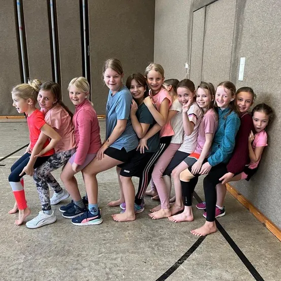 Eine Gruppe junger Mädchen in Sportbekleidung steht zusammen, lächelt und posiert für ein Foto in einer Turnhalle.