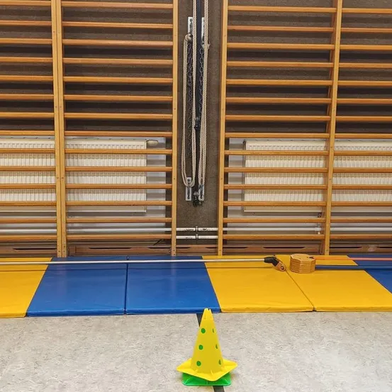 Ein gelber Kegel steht auf einem gefliesten Boden vor Holzregalen, wobei der Boden mit blauen und gelben Matten bedeckt ist.