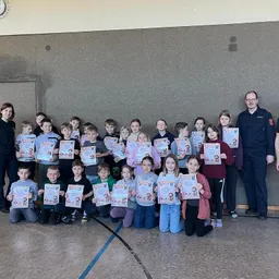 Eine Gruppe von Kindern und zwei Erwachsenen halten Urkunden und posieren für ein Foto in einem Raum.