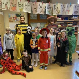 Eine Gruppe von Kindern in verschiedenen Kostümen posiert für ein Foto in einem Klassenzimmer mit Dekorationen an der Wand.