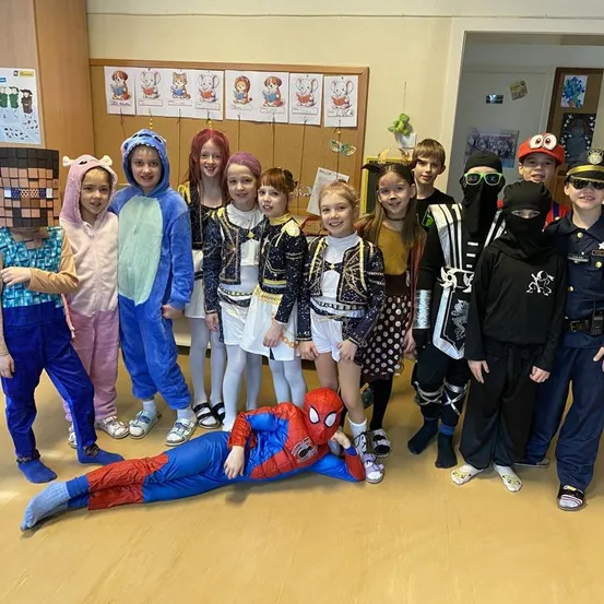 Eine Gruppe von Kindern in Kostümen posiert für ein Foto in einem Raum. Ein Kind liegt in einem Spider-Man-Kostüm auf dem Boden.
