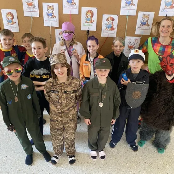 Kinder in verschiedenen Kostümen, darunter Militär- und Tieroutfits, posieren für ein Gruppenfoto mit einem lächelnden Erwachsenen in einem Clown-Kostüm.