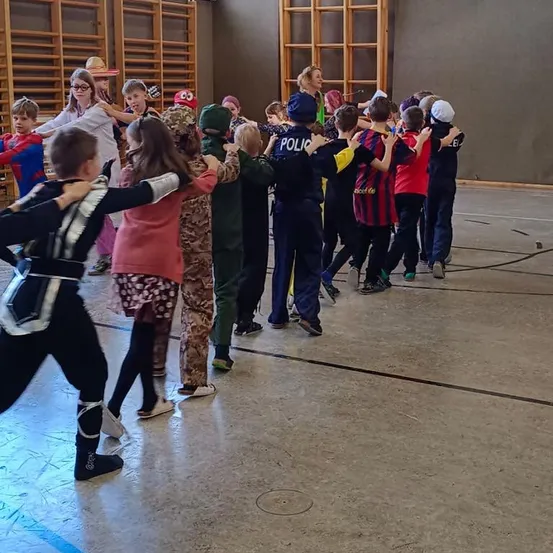 Eine Gruppe von Kindern in verschiedenen Kostümen steht in einer Reihe und scheint einen Tanz zu üben.