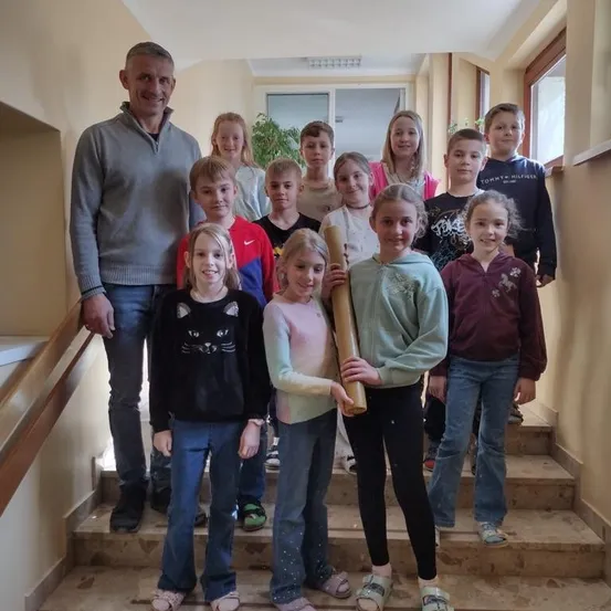Eine Gruppe von Kindern und einem Mann stehen auf einer Treppe und lächeln für ein Foto. Der Mann trägt ein graues Sweatshirt, während die Kinder verschiedene Kleidungsstücke tragen.