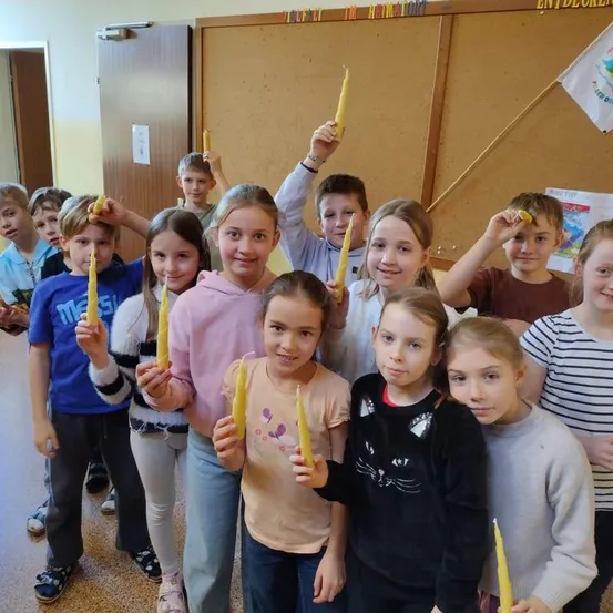 Eine Gruppe von Kindern im Klassenzimmer, lächelnd und gelbe Kerzen haltend. Sie posieren für ein Foto.