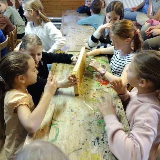 Eine Gruppe junger Mädchen arbeitet an einem Projekt an einem Tisch, einige mit Farbe an Händen und Kleidung. Einige sitzen, andere stehen.