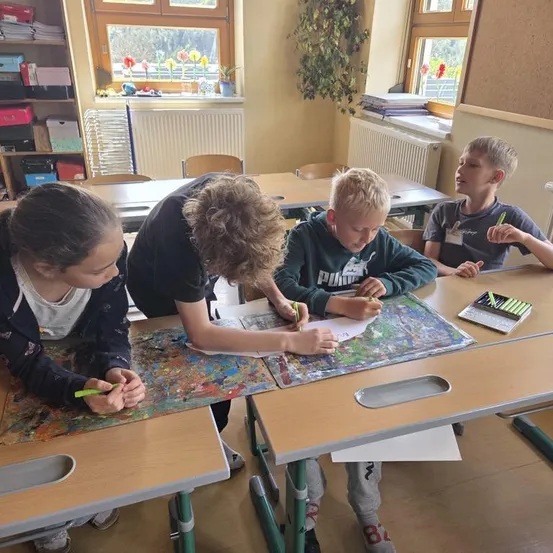 Vier Schüler sitzen in einem Klassenzimmer an einem Tisch und beschäftigen sich mit einer Malaktivität. Sie haben Marker und ein Malbuch vor sich geöffnet.