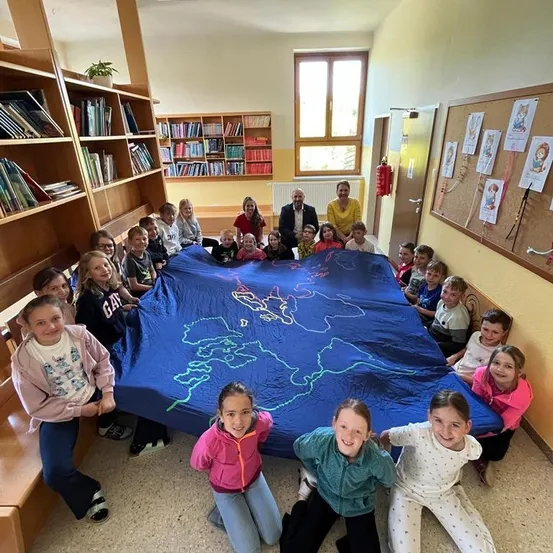 Eine Gruppe von Kindern und Erwachsenen versammelt sich in einem Raum und sitzt um eine große blaue Karte auf dem Boden herum. Sie lächeln und posieren für ein Foto.