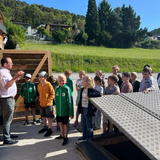 Eine Gruppe von Kindern in grünen und weißen Trikots hört einem Mann in einem weißen Hemd zu, der vor einem Holztor steht.