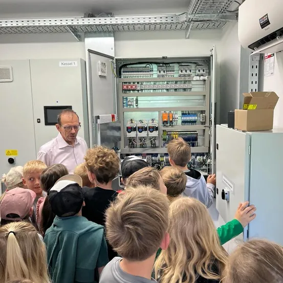 Ein Mann erklärt einer Gruppe von Kindern etwas über ein Schalttafel in einem Raum.