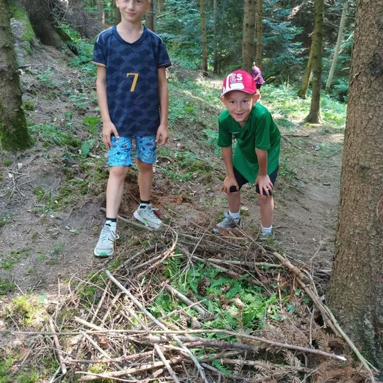 Zwei Jungen stehen auf einem Waldweg, einer trägt ein blaues Shirt mit der Nummer 7 und der andere ein grünes Shirt und eine rote Kappe.