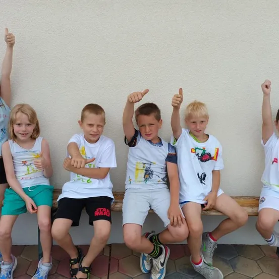 Fünf Kinder sitzen auf einer Bank und geben alle einen Daumen hoch. Der Junge auf der rechten Seite hat eine Star Wars-Aufschrift auf der Shorts.