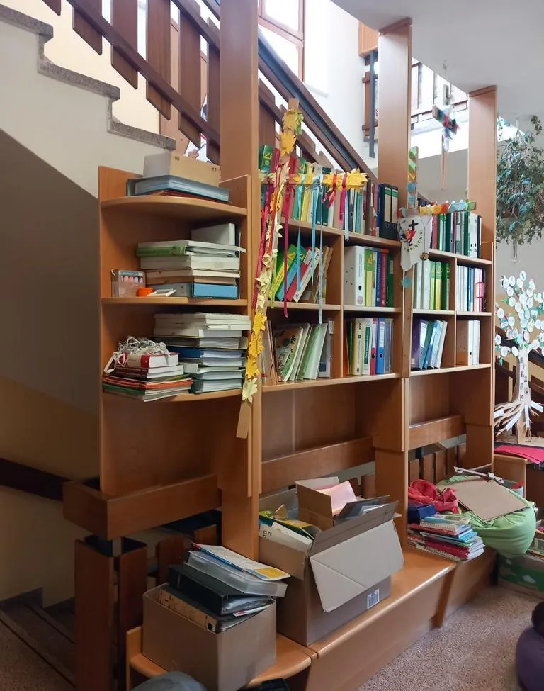 Ein hölzerne Bücherregal gefüllt mit Büchern und Ordnern, mit bunten Bändern und einer Pflanze auf der rechten Seite.