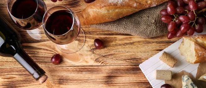 Eine Flasche Wein, zwei Weingläser und ein Laib Brot mit Trauben auf einem Holztisch.