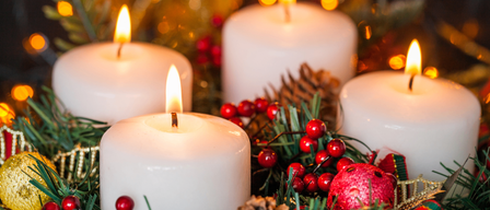 Eine Nahaufnahme mehrerer brennender weißer Kerzen mit roten Beeren und Tannenzapfen darum. Die Kerzen strahlen warm und sind von Weihnachtsdekoration umgeben.