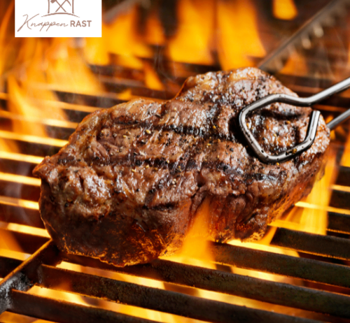 Ein Steak wird über offenem Feuer gegrillt und von einer Metallzange gehalten.