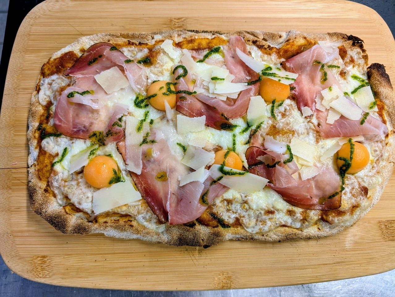 Eine Pizza mit Schinken, Käse und ein paar Eiern, auf einem Holzschneidebrett platziert.