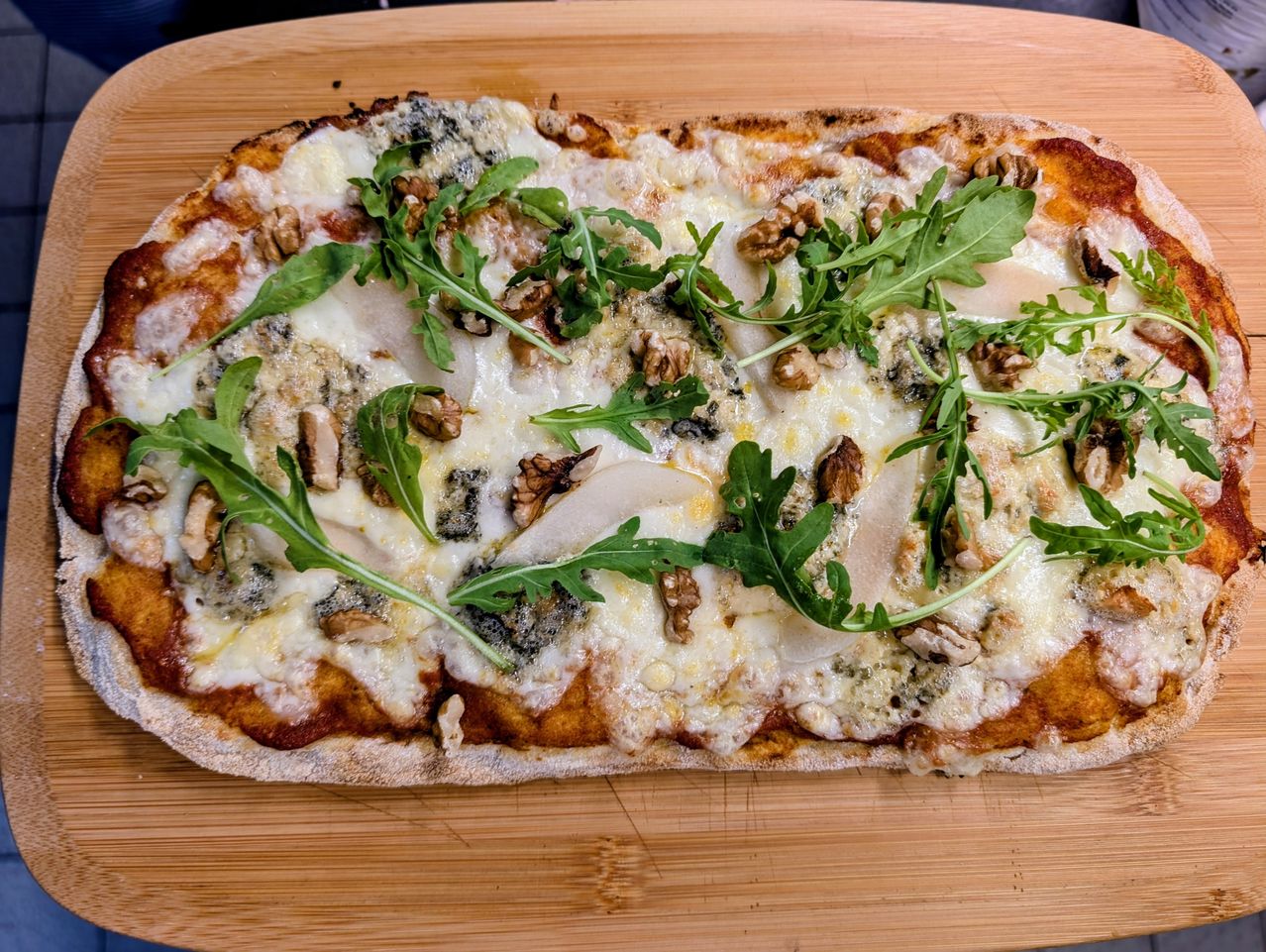A flatbread pizza topped with blue cheese, walnuts, and arugula on a wooden board.
