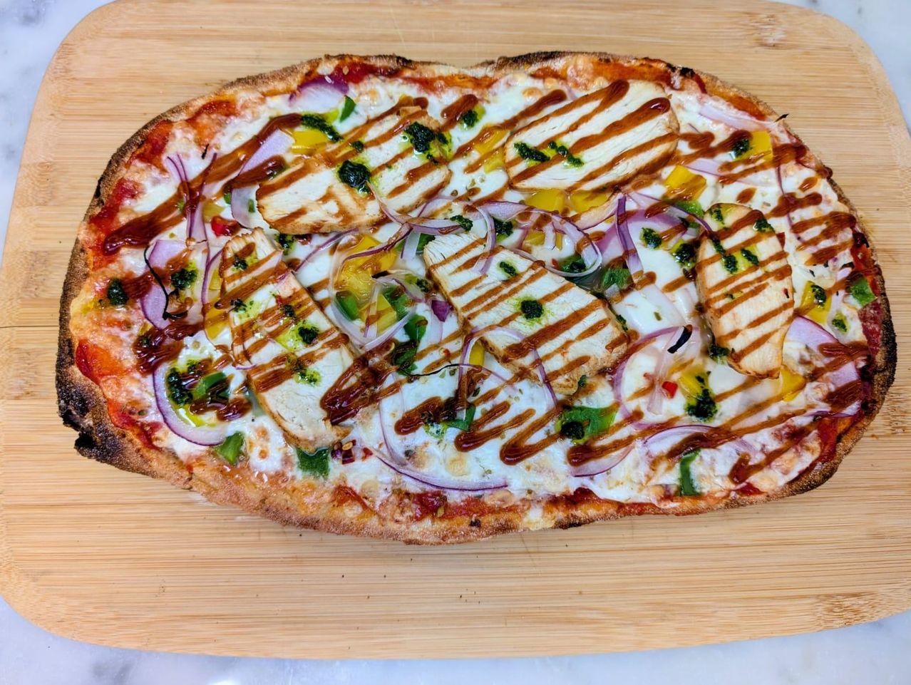 A pizza with grilled chicken, red onions, and a drizzle of sauce on a wooden board.