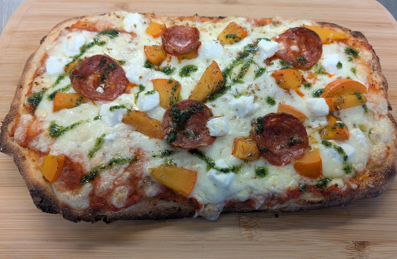 A close-up view of a pizza topped with sliced tomatoes, mozzarella cheese, and green pesto.