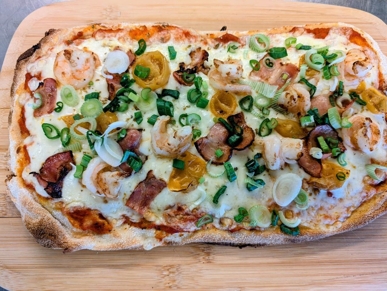 Eine Pizza mit Garnelen, Speck, Pilzen und Frühlingszwiebeln mit geschmolzenem Käse.
