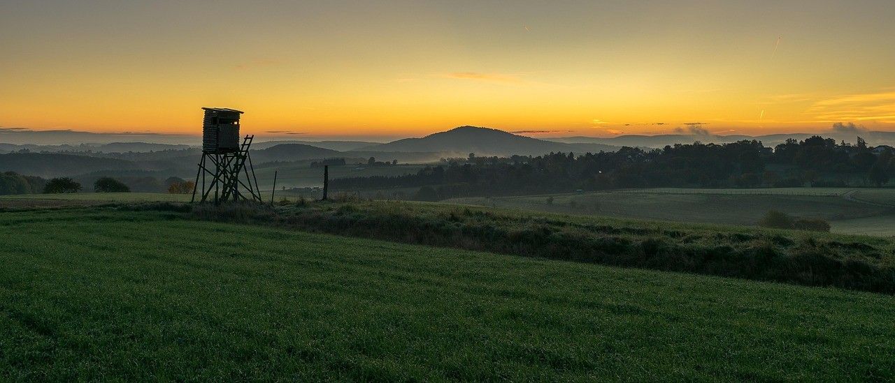 Ein Wachturm steht allein auf einer Wiese bei untergehender Sonne und einer Bergkette in der Ferne.