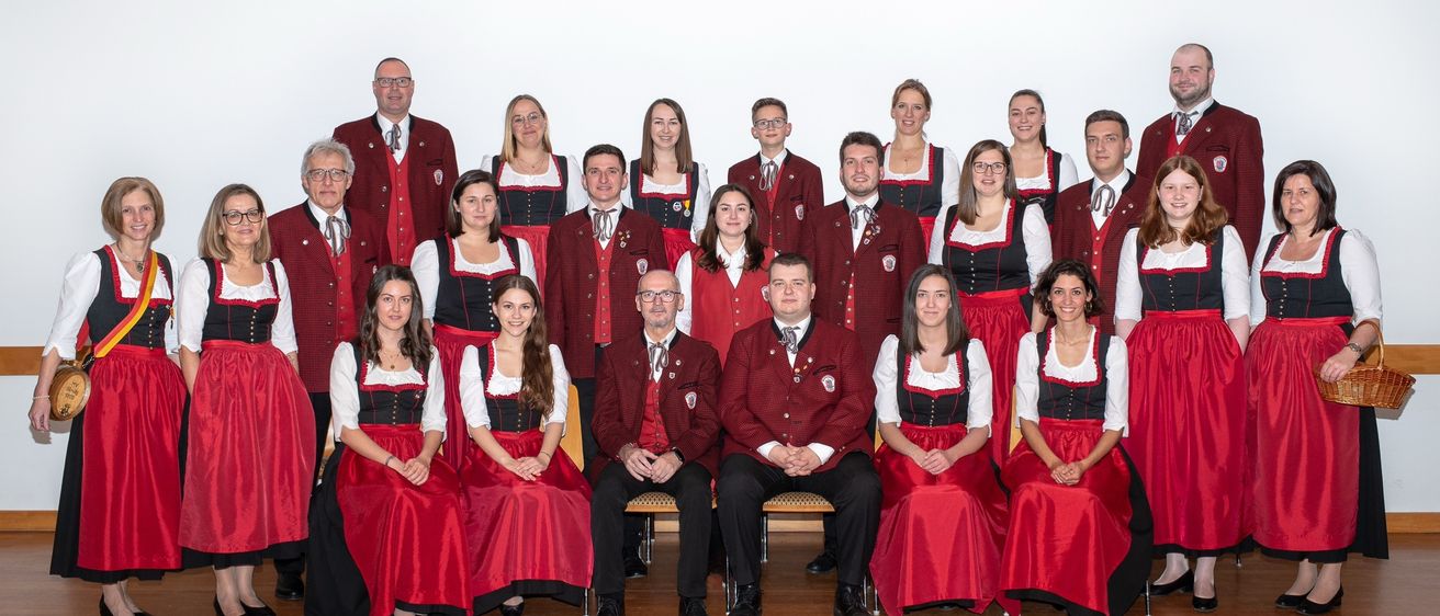 Eine Gruppe von Menschen in traditioneller bayerischer Kleidung, mit Männern und Frauen, posiert für ein Foto im Studio.