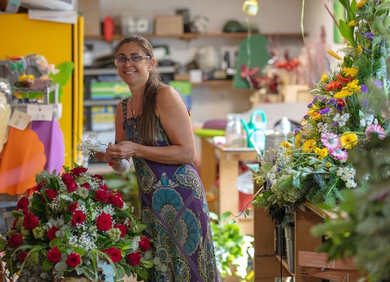 Eine Frau in einem Blumenkleid arrangiert einen Strauß roter Rosen und anderer Blumen in einem Blumenladen.