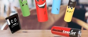 Fünf Batterien in verschiedenen Farben und Größen schweben auf einem Holztisch. Jede Batterie hat ein einzigartiges Gesicht darauf gezeichnet. Die rote Batterie hat ein lächelndes Gesicht. Die blaue Batterie hat ein überraschtes Gesicht. Die grüne Batterie hat ein trauriges Gesicht. Die gelbe Batterie hat ein schockiertes Gesicht. Die schwarze Batterie hat ein wütendes Gesicht.