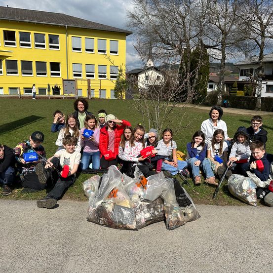 Eine Gruppe von Menschen sitzt auf einem Rasen mit Säcken voller Müll vor einem gelben Gebäude. Sie posieren für ein Foto.