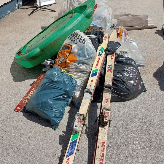 Eine Ansammlung von weggeworfenen Gegenständen, darunter ein grünes Kajak, Skier und Plastiktüten, sind auf dem Boden verstreut.