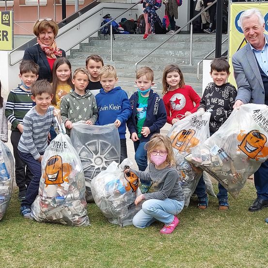 Kinder und Erwachsene halten Müllsäcke voller Abfall, lächeln und posieren für ein Foto vor einer Treppe.