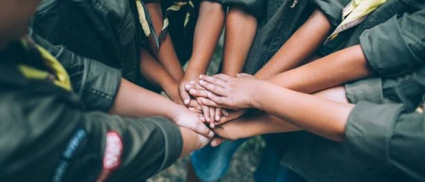 Eine Gruppe von Kindern in Pfadfinderuniformen, die ihre Hände in einem Kreis aufeinanderlegen.
