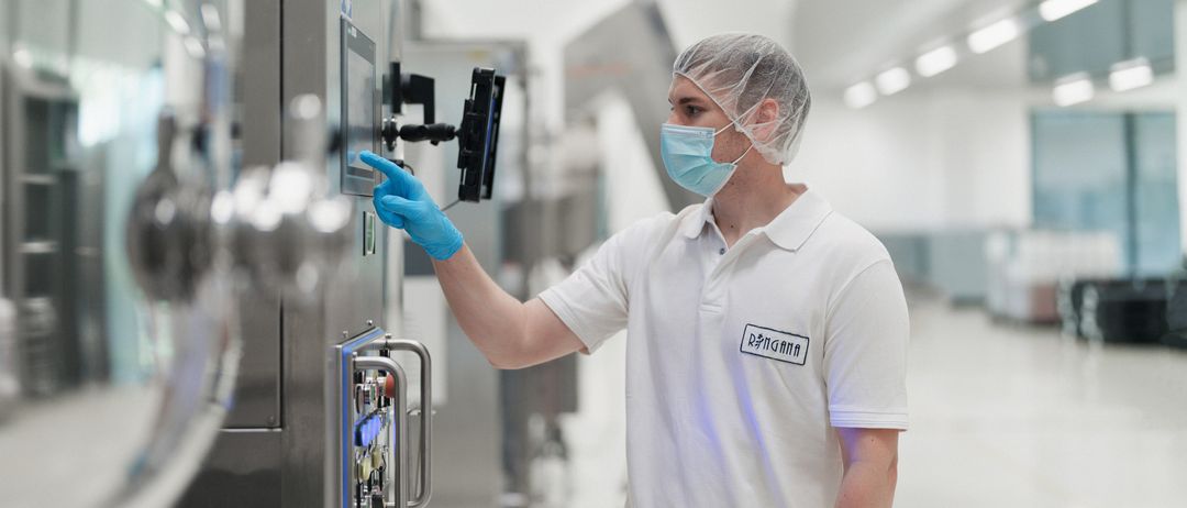 Ein Mann in Laborkittel und Gesichtsmaske bedient eine Kontrolltafel in einem Labor.